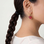 Close-up of a person wearing a red strawberry charm earring with a white background