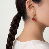 Close-up of a person wearing a red strawberry charm earring with a white background