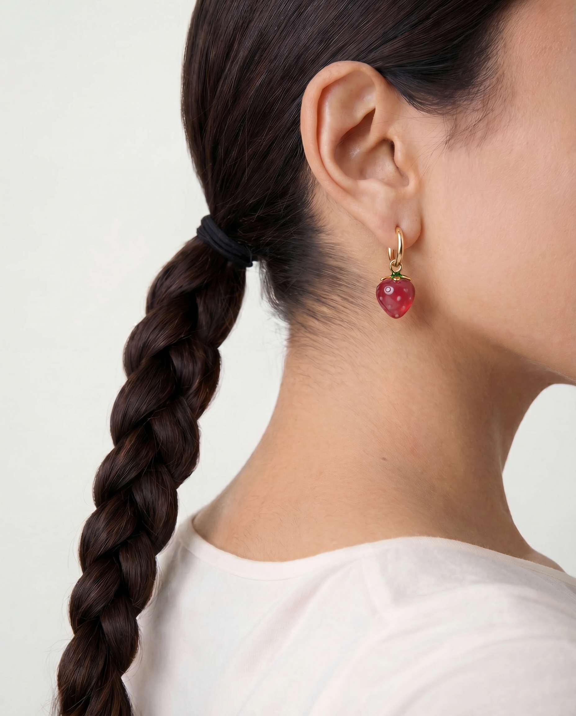 Close-up of a person wearing a red strawberry charm earring with a white background