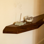 Incense stick with a glass ashtray on a wooden shelf against a beige wall.