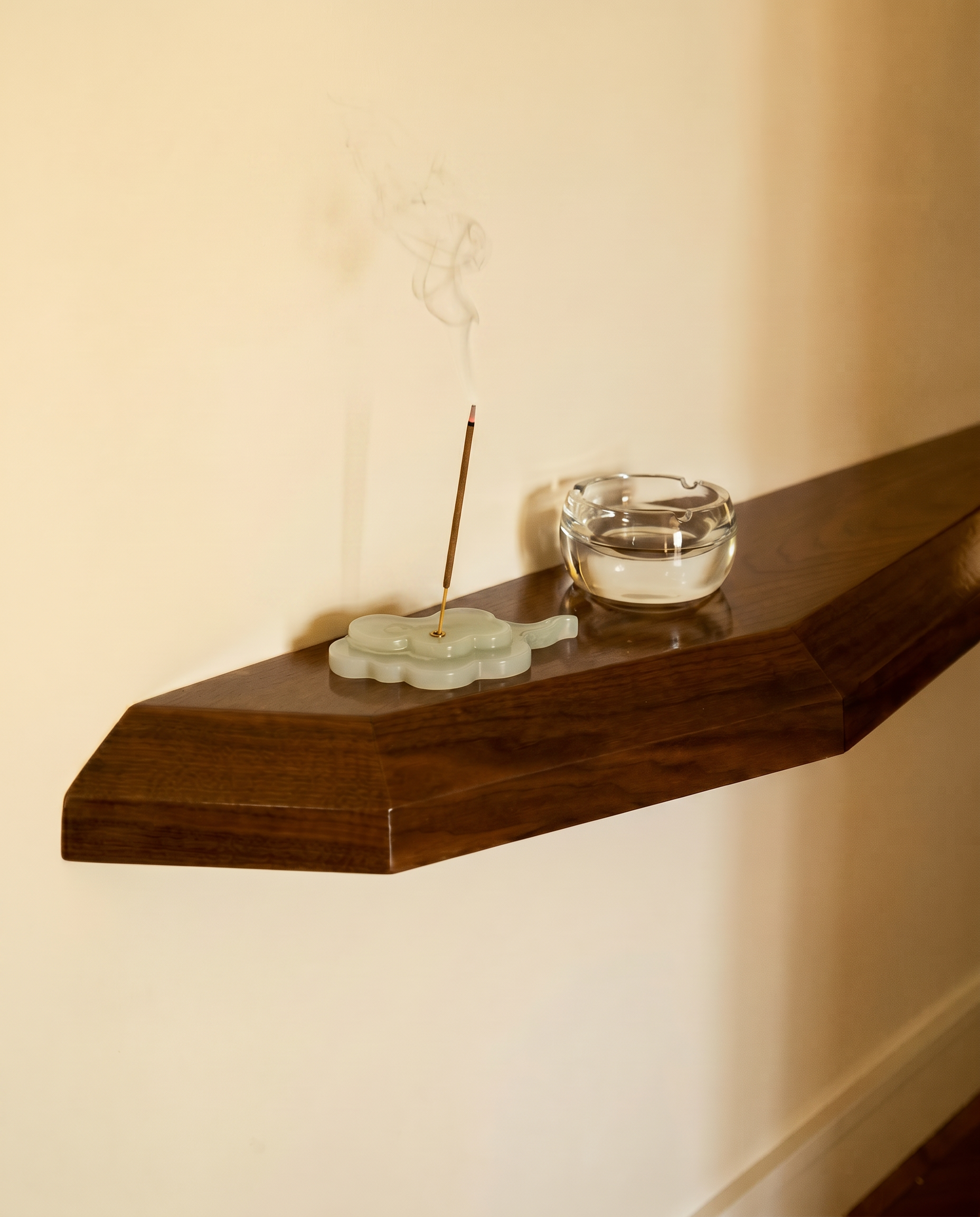 Incense stick with a glass ashtray on a wooden shelf against a beige wall.