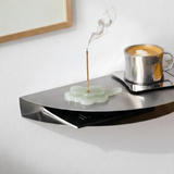 Modern wall-mounted shelf with a cup of coffee and incense stick on a white wall.