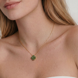 Close-up of a woman wearing a gold necklace with a green clover-shaped jade pendant.