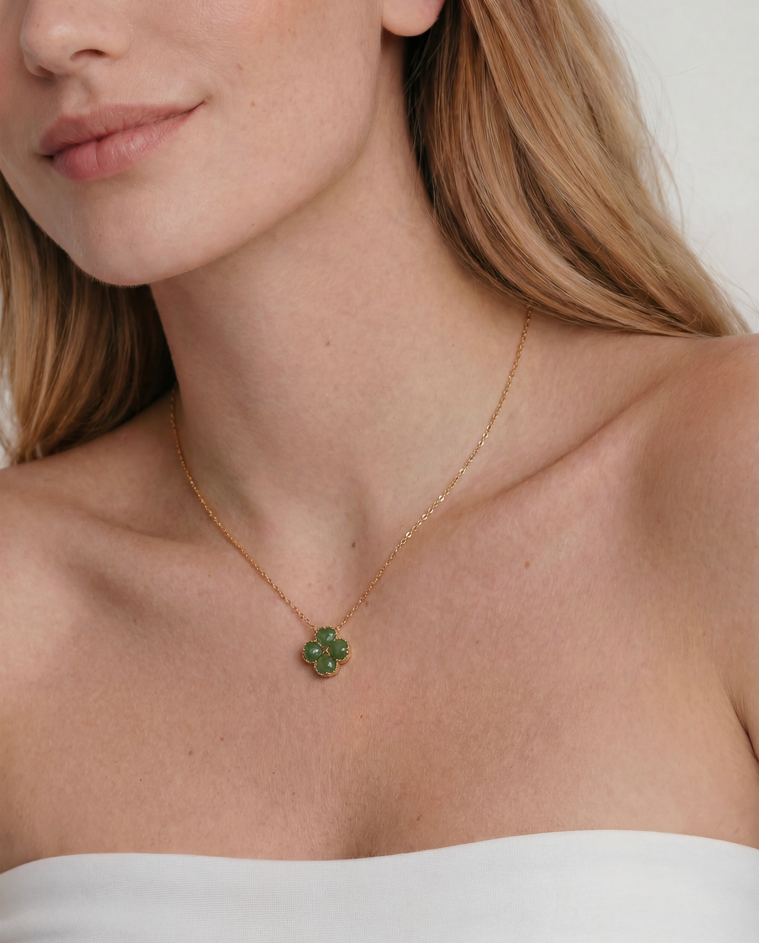 Close-up of a woman wearing a gold necklace with a green clover-shaped jade pendant.