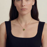 Woman wearing a black tank top and a necklace with a green clover-shaped jade pendant on a beige background