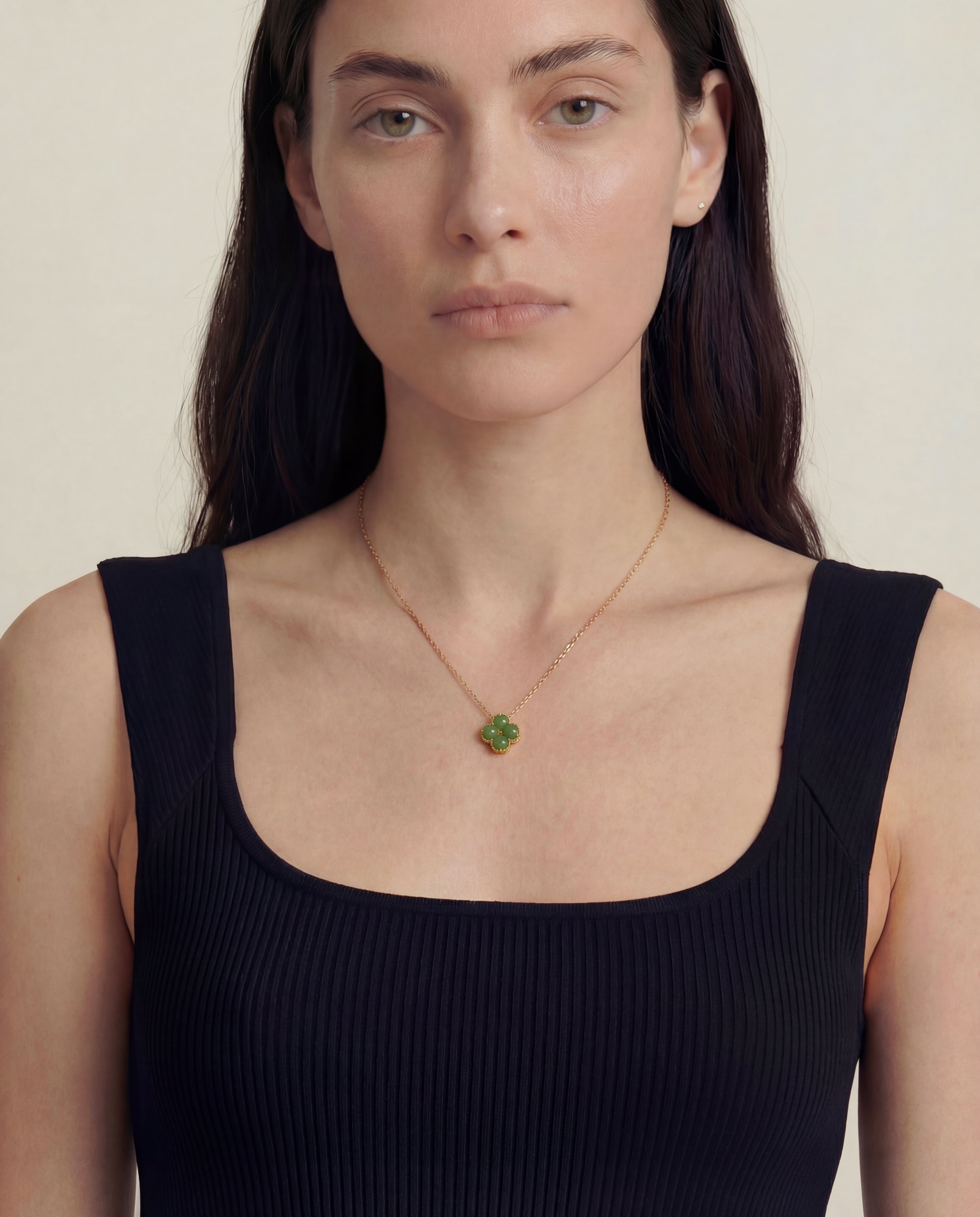 Woman wearing a black tank top and a necklace with a green clover-shaped jade pendant on a beige background