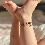 Child wearing a pink strawberry quartz peace buckle anklet with cherry charm while resting on a bed.