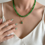 Person wearing a green beaded necklace with a pendant, set against a neutral background.