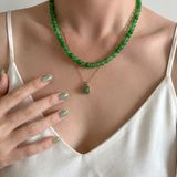 Person wearing a green beaded necklace with a pendant, set against a neutral background.
