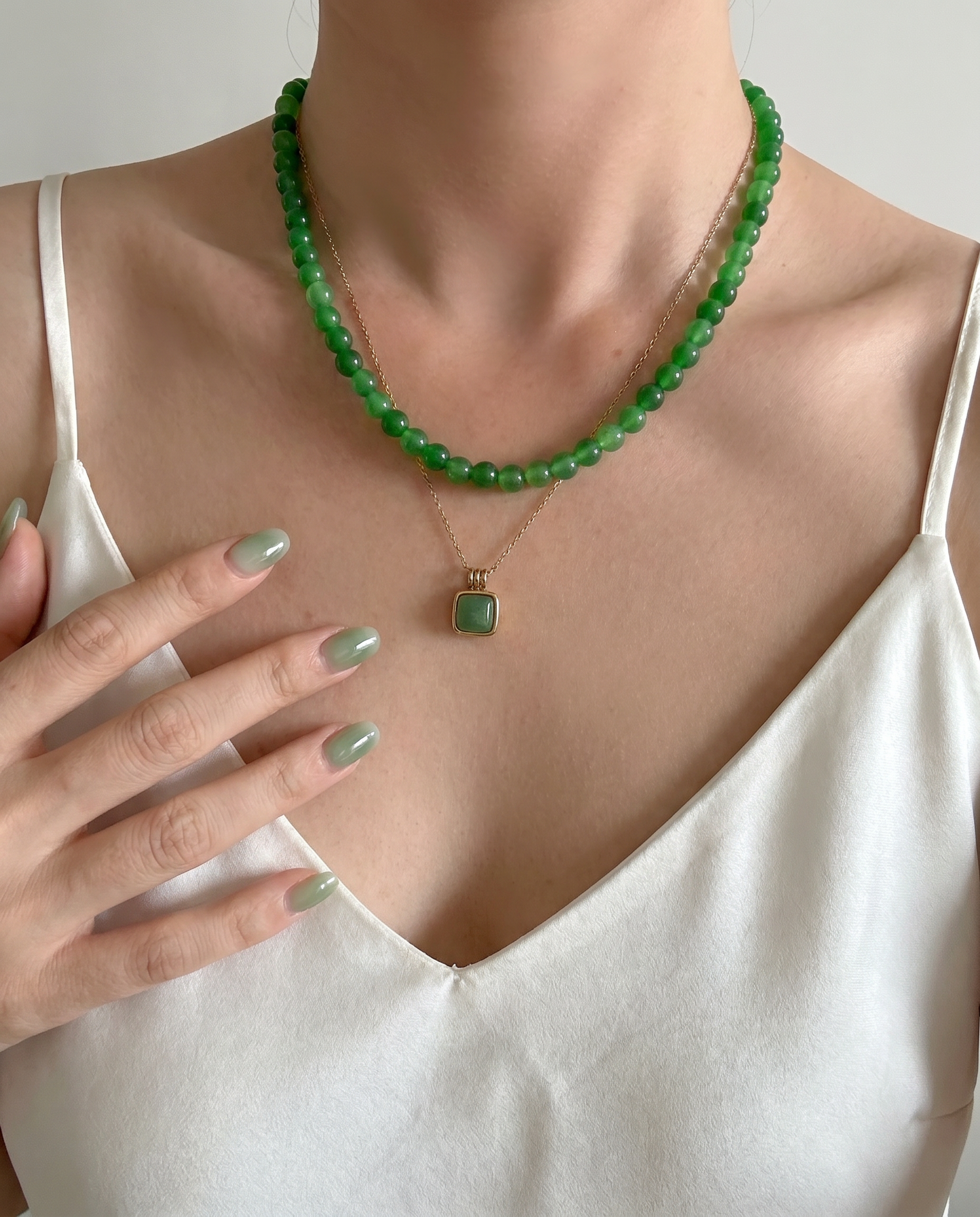 Person wearing a green beaded necklace with a pendant, set against a neutral background.