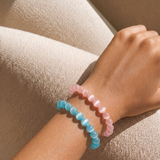 Close-up of a wrist wearing two colorful beaded bracelets on a beige fabric background