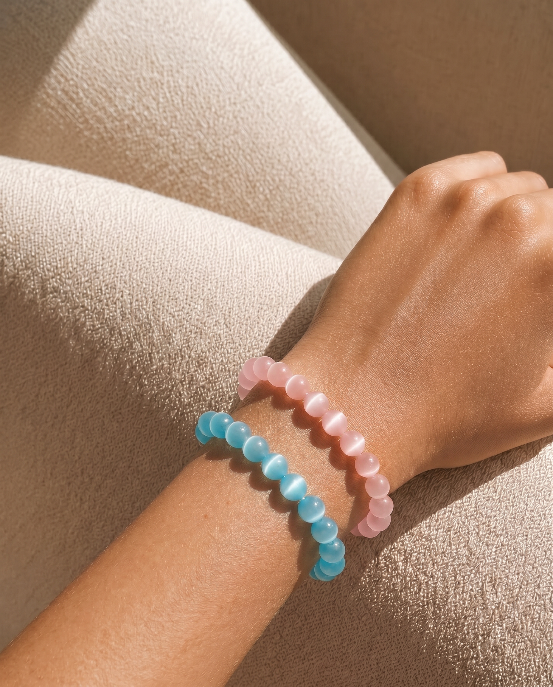 Close-up of a wrist wearing two colorful beaded bracelets on a beige fabric background