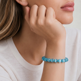 Woman wearing a blue beaded bracelet on a plain background