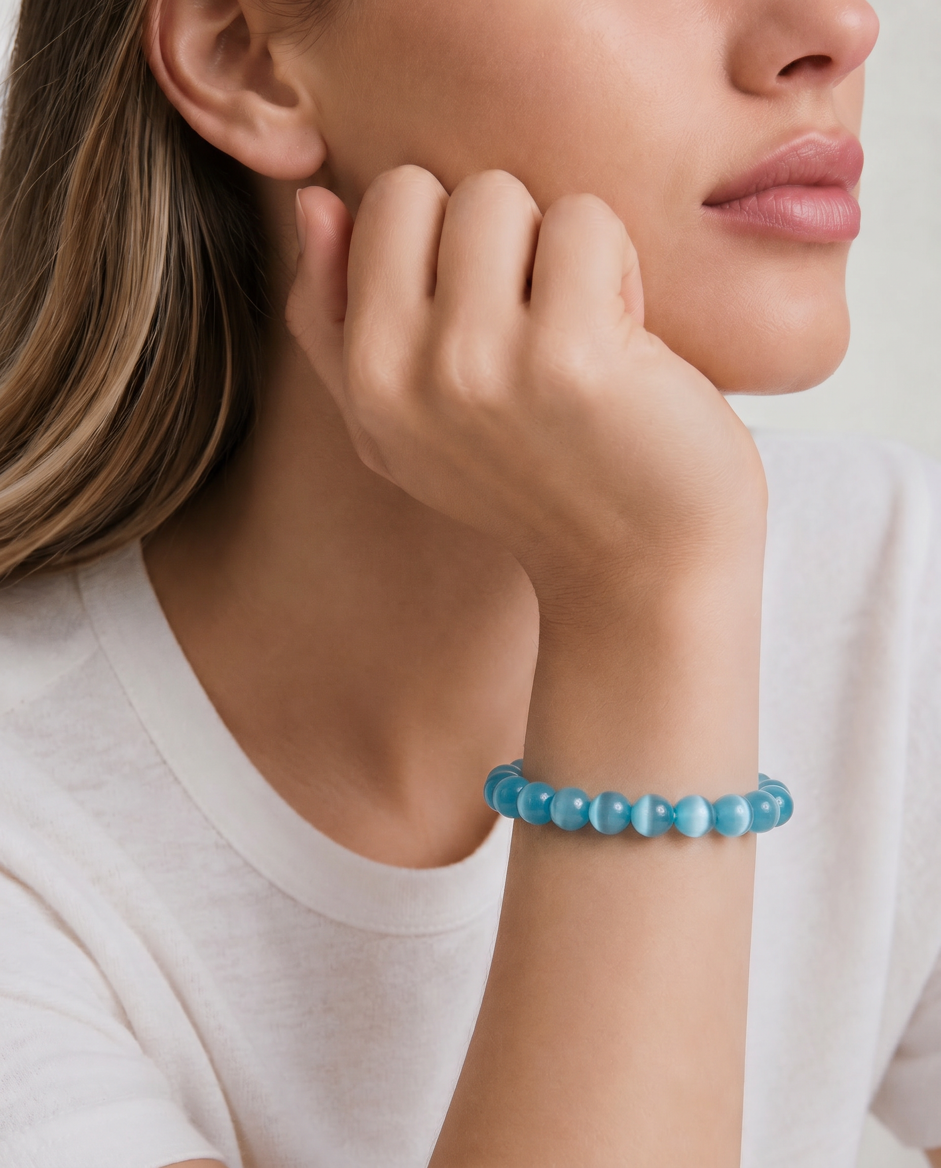 Woman wearing a blue beaded bracelet on a plain background