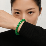 Person wearing a green beaded bracelet on a plain background