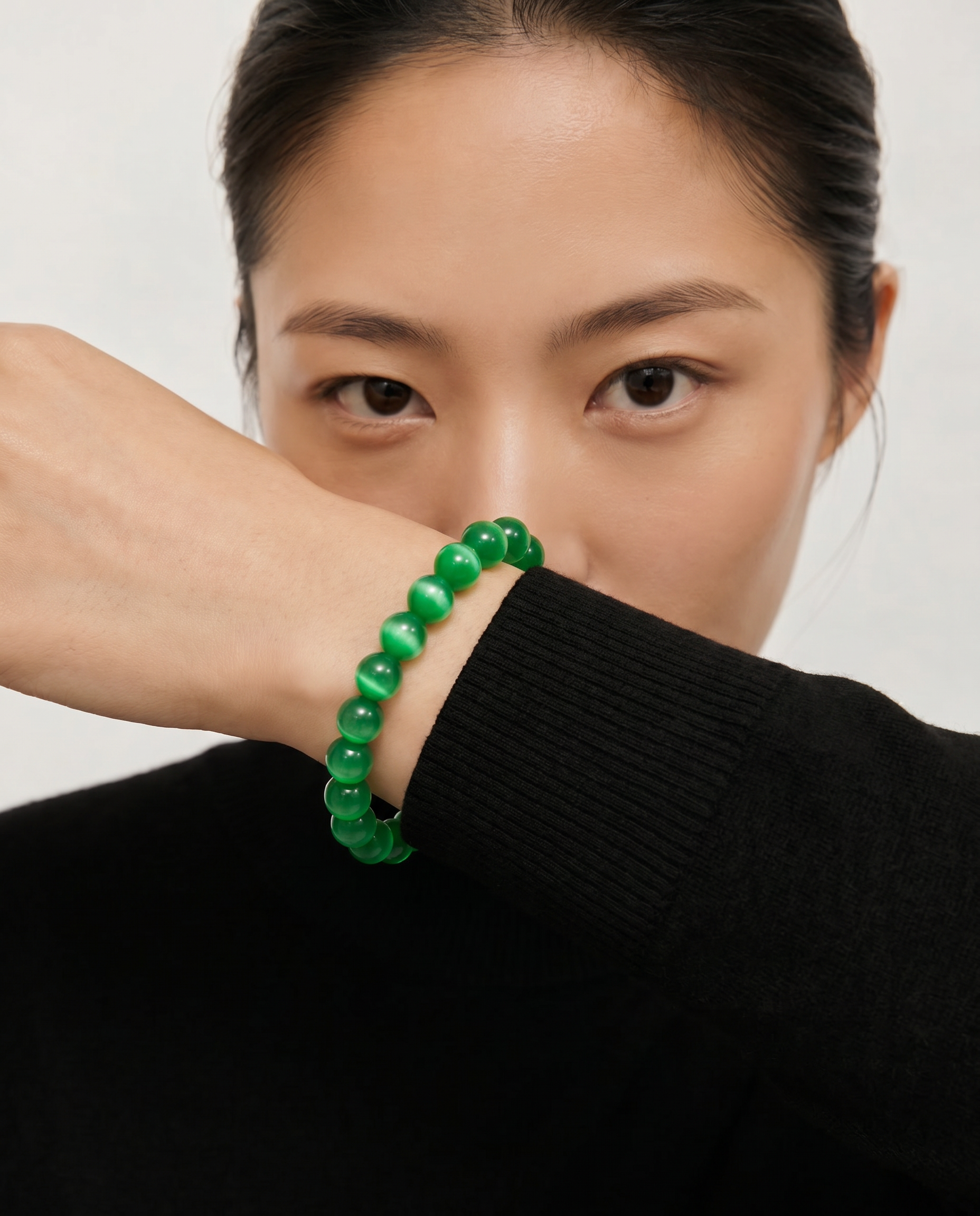 Person wearing a green beaded bracelet on a plain background