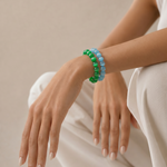 Person wearing green and blue beaded bracelets on a neutral background