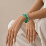 Person wearing green and blue beaded bracelets on a neutral background