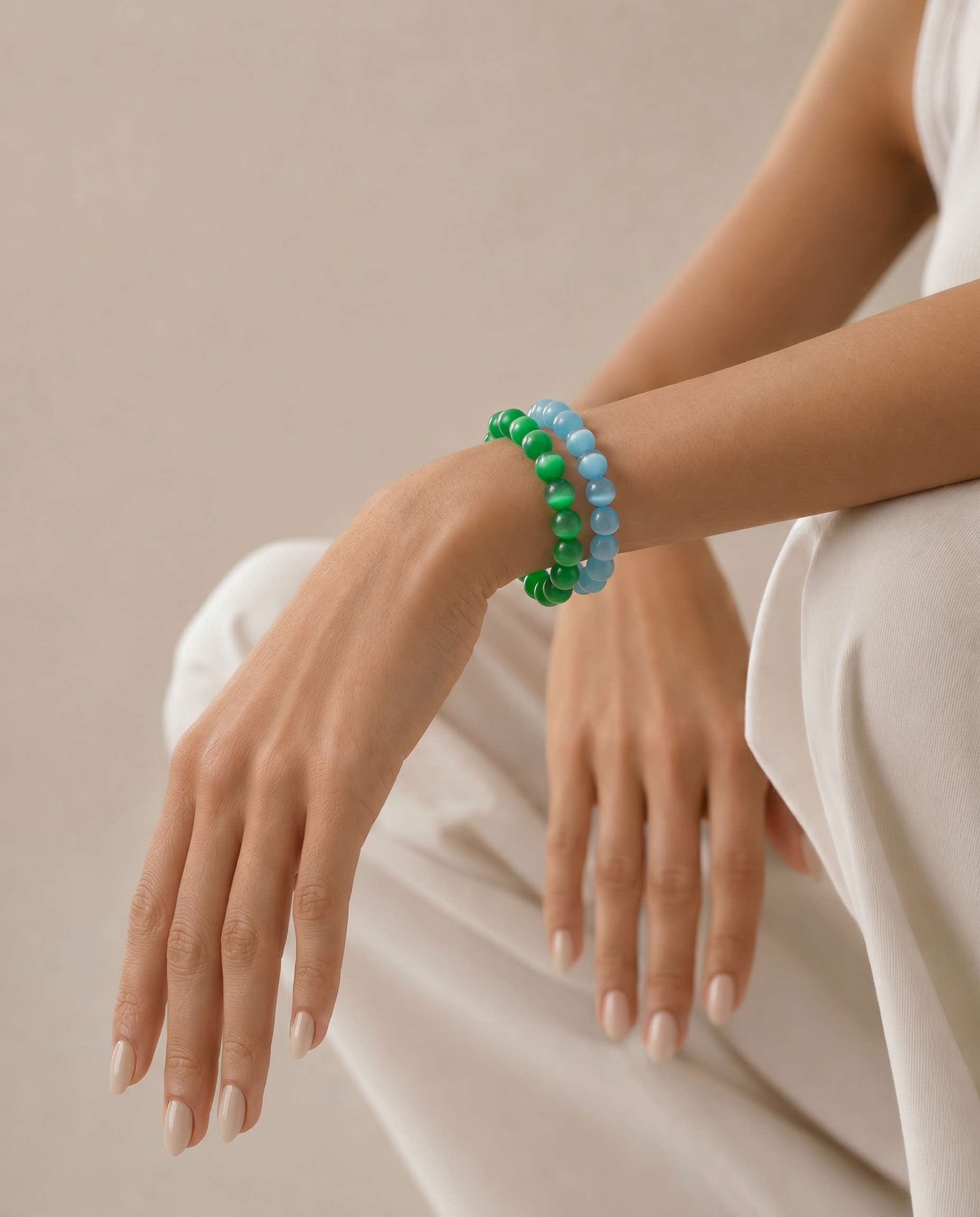 Person wearing green and blue beaded bracelets on a neutral background