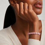 Close up of a woman wearing a pink beaded bracelet on a neutral background