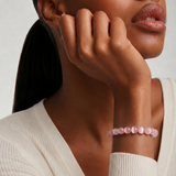 Close up of a woman wearing a pink beaded bracelet on a neutral background