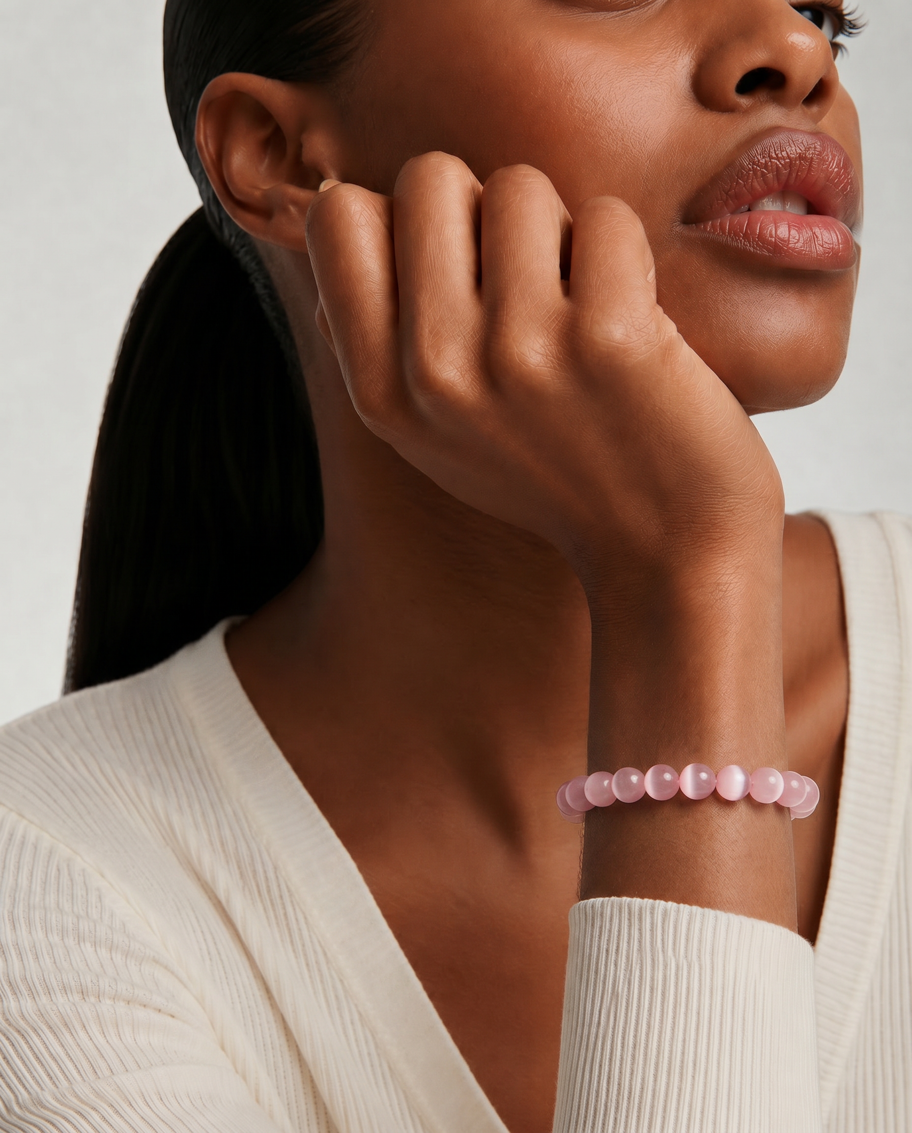 Close up of a woman wearing a pink beaded bracelet on a neutral background