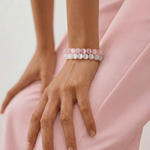Person wearing two beaded bracelets on a light pink background