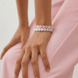 Person wearing two beaded bracelets on a light pink background