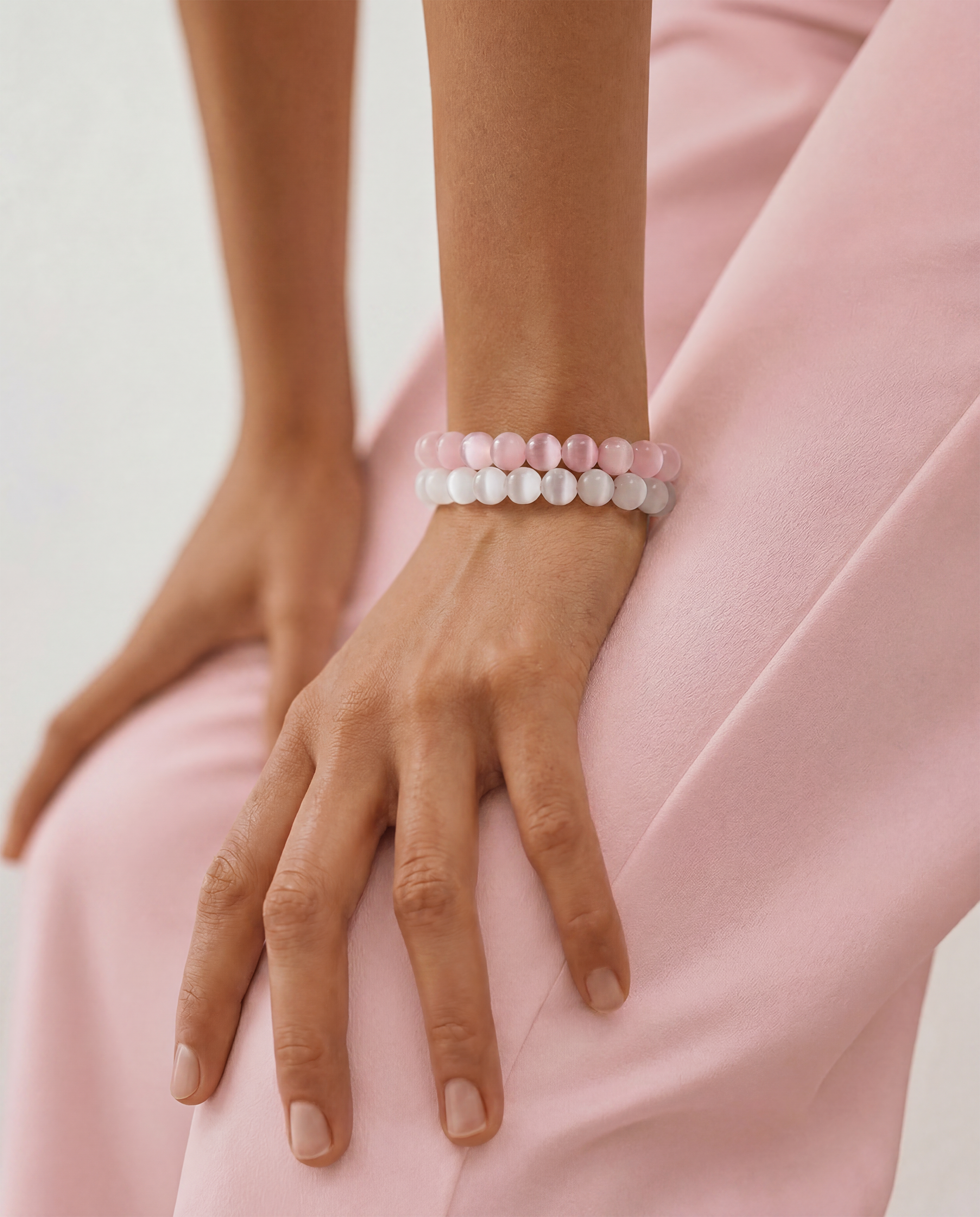 Person wearing two beaded bracelets on a light pink background