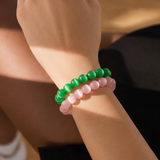 Close-up of a wrist wearing two beaded bracelets, one green and one pink, on a blurred background.