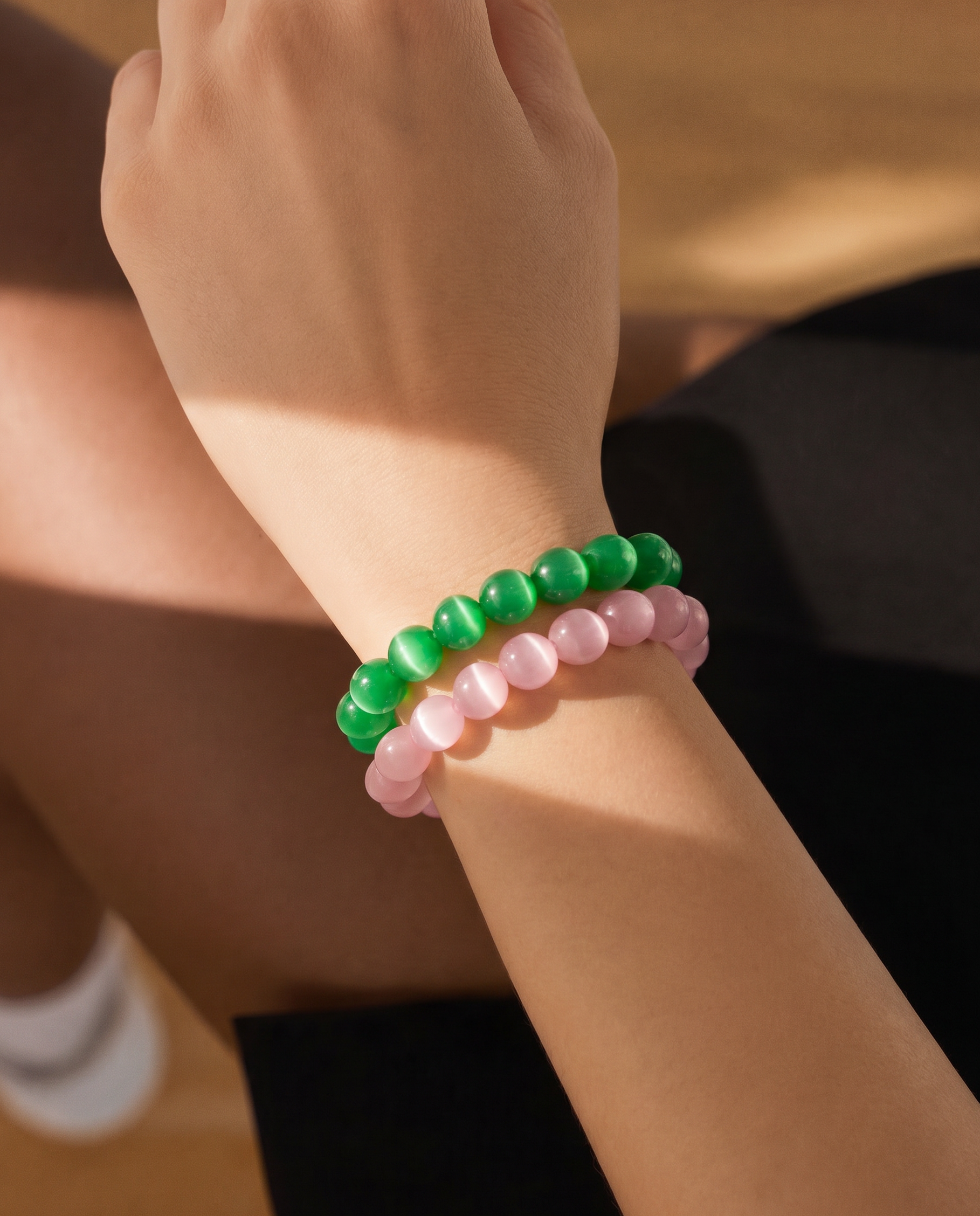 Close-up of a wrist wearing two beaded bracelets, one green and one pink, on a blurred background.