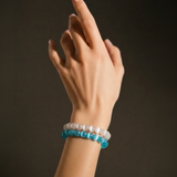 Hand wearing a blue beaded bracelet and white beaded bracelet on a dark background