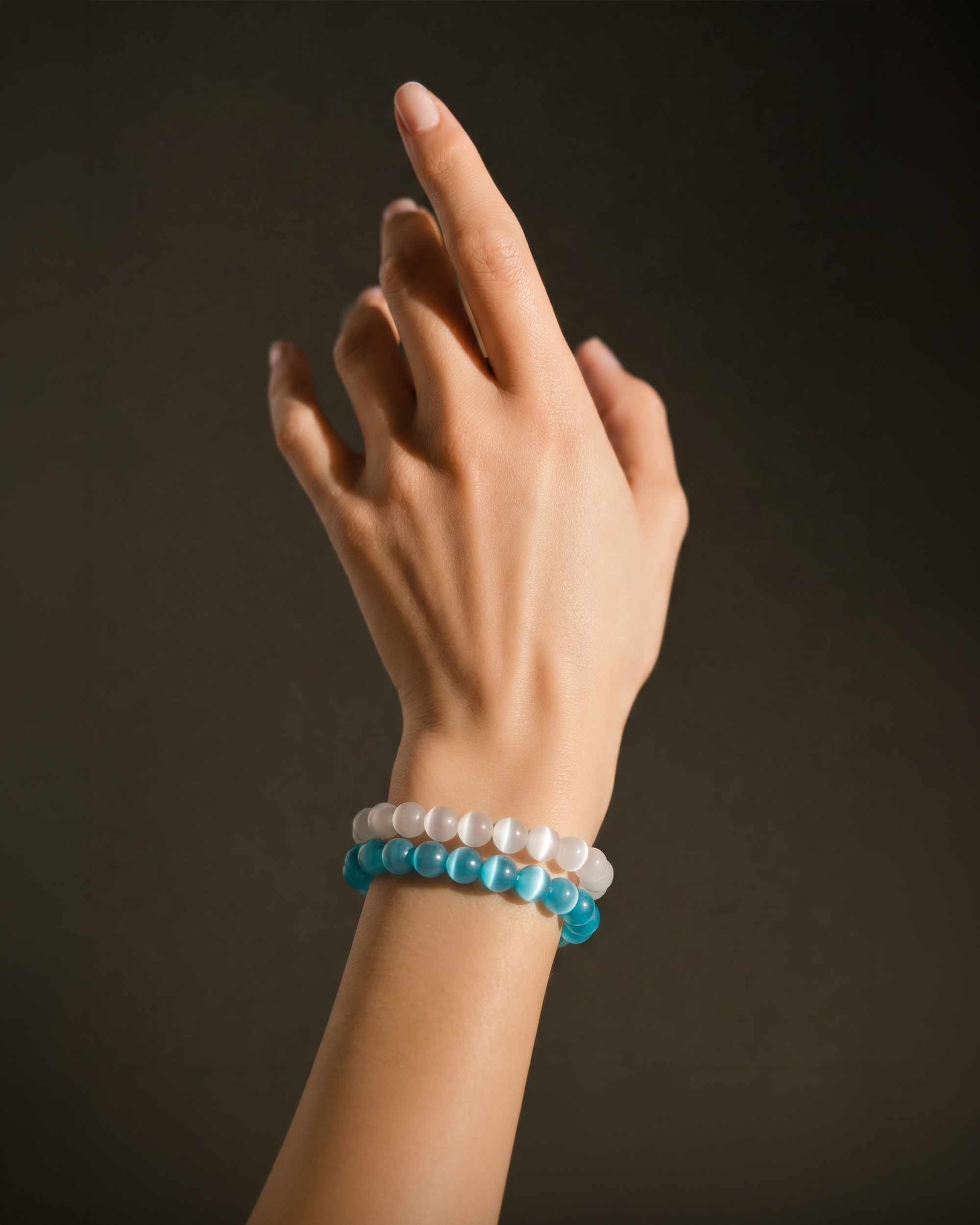 Hand wearing a blue beaded bracelet and white beaded bracelet on a dark background