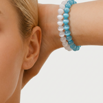 Close-up of a person wearing a blue and white beaded bracelet on a plain background