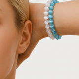 Close-up of a person wearing a blue and white beaded bracelet on a plain background