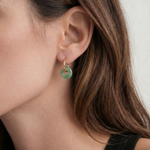 Close-up of an ear wearing a green jade hoop earring with a neutral background