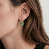 Close-up of an ear wearing a green jade hoop earring with a neutral background