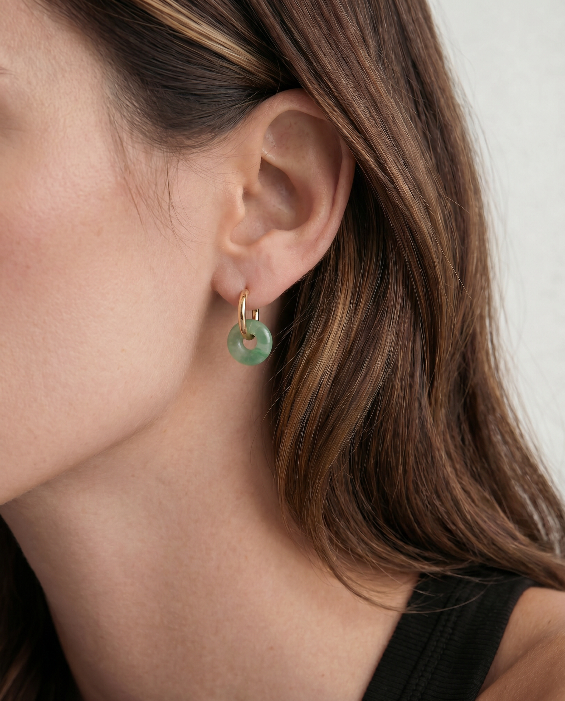 Close-up of an ear wearing a green jade hoop earring with a neutral background