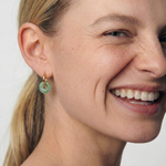 Close-up of a woman wearing a green jade hoop earring with a plain background 
