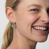 Close-up of a woman wearing a green jade hoop earring with a plain background 