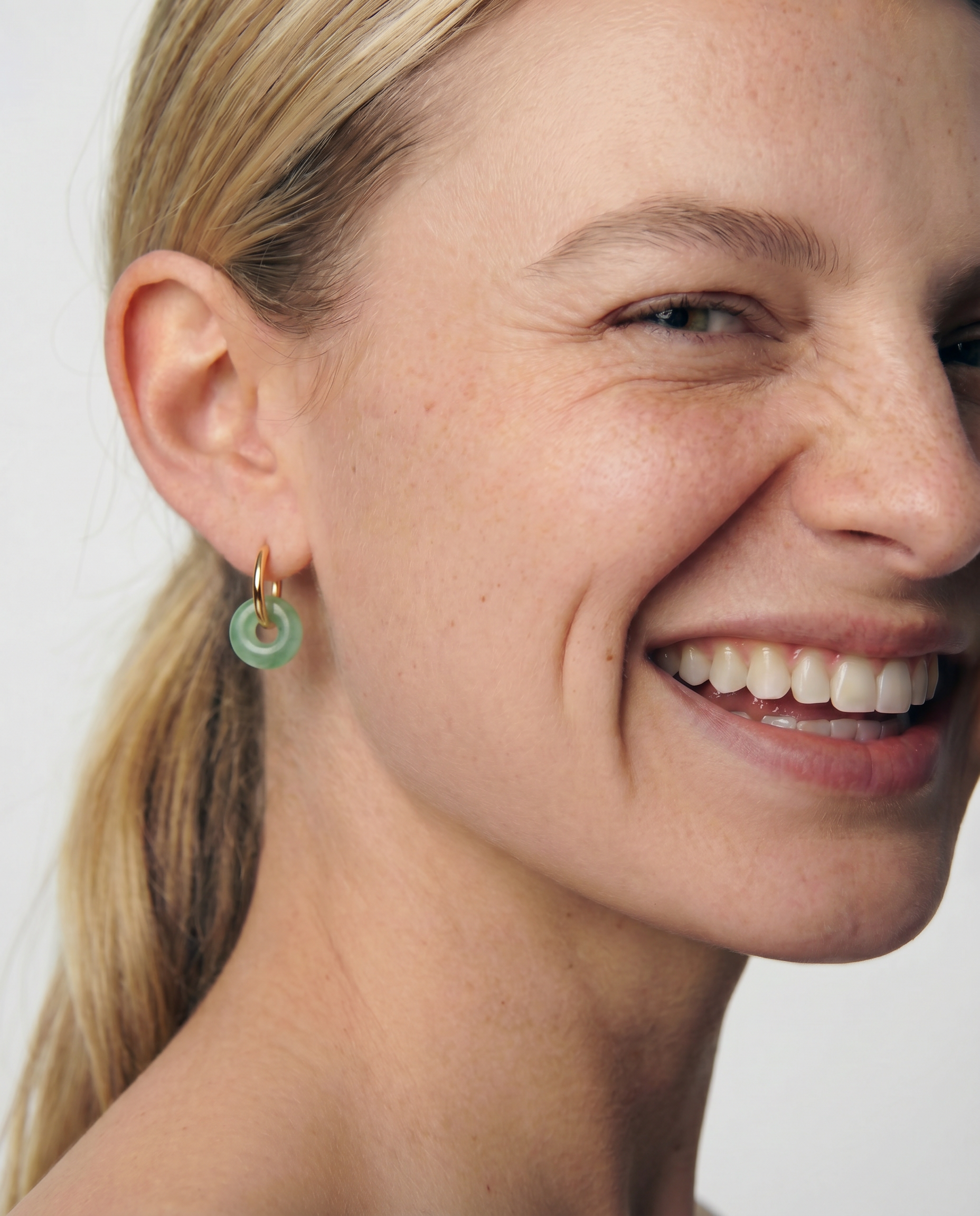 Close-up of a woman wearing a green jade hoop earring with a plain background 