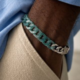 Close-up of a person's arm wearing a teal chain bracelet with a blue sleeve.