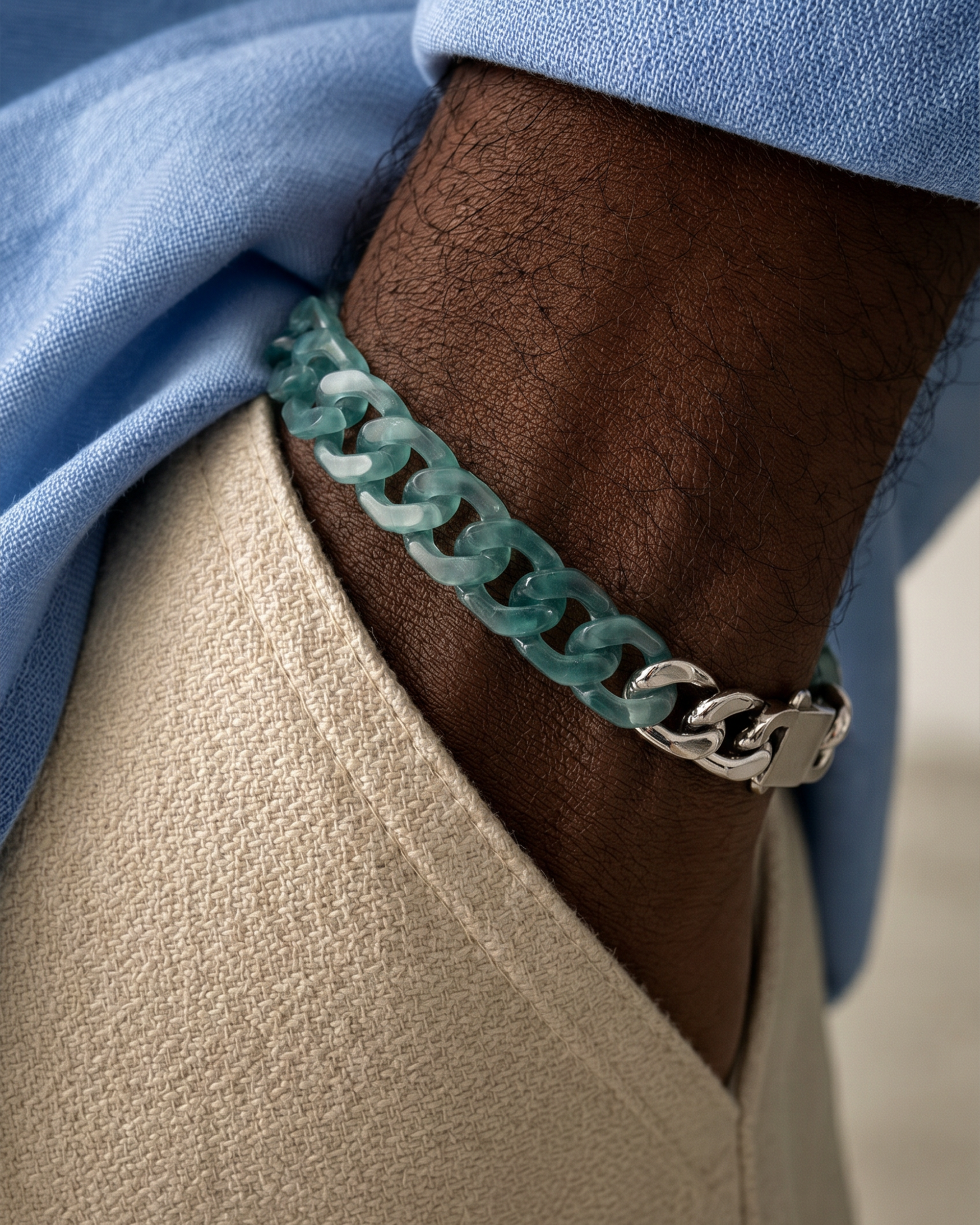 Close-up of a person's arm wearing a teal chain bracelet with a blue sleeve.