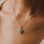 Close-up shot of a necklace with a heart-shaped green pendant on a person's neck