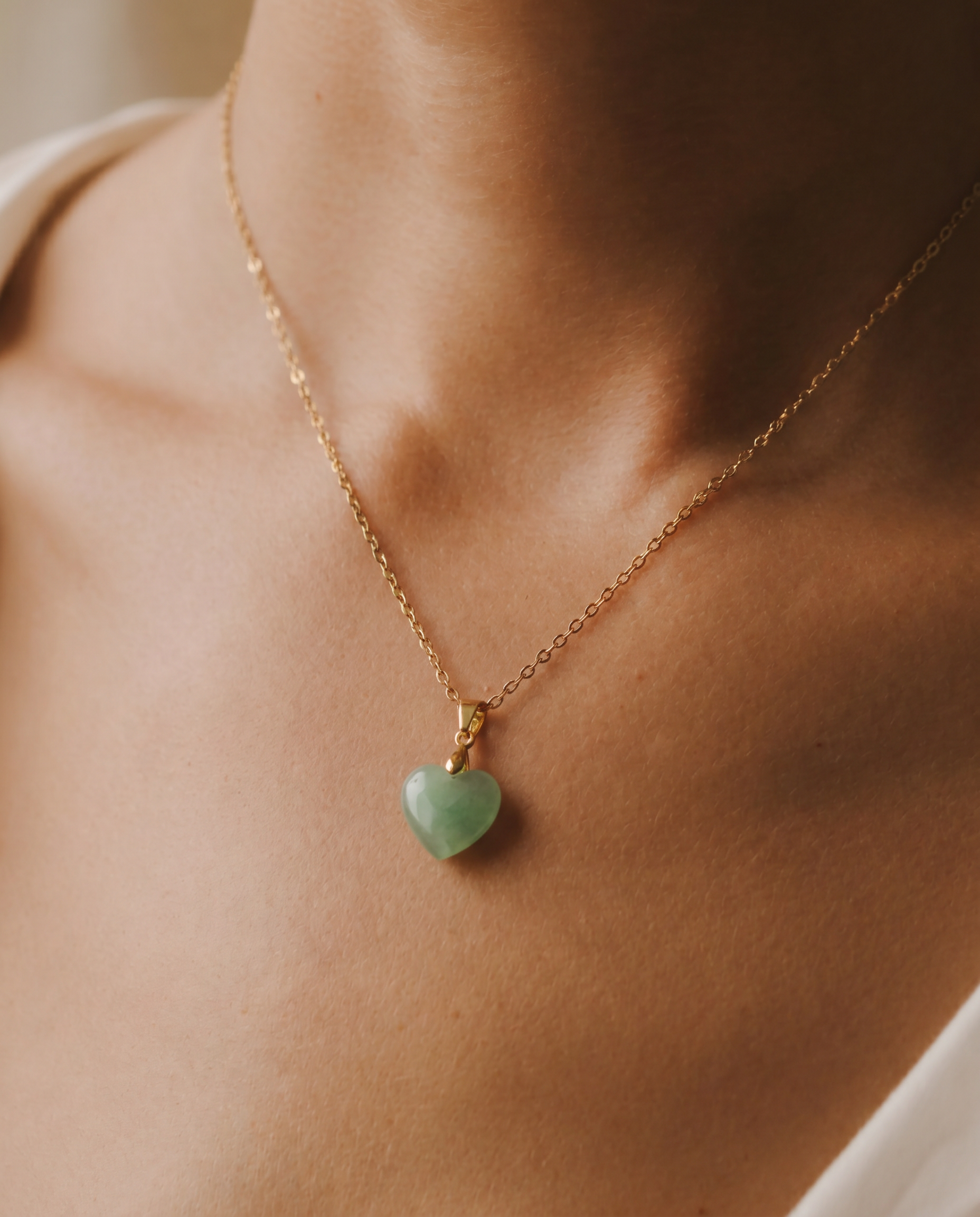 Close-up shot of a necklace with a heart-shaped green pendant on a person's neck