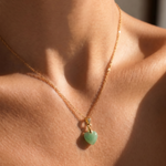 Close-up of a necklace with a tiny green heart-shaped pendant on a person's neck