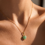 Close-up of a necklace with a tiny green heart-shaped pendant on a person's neck