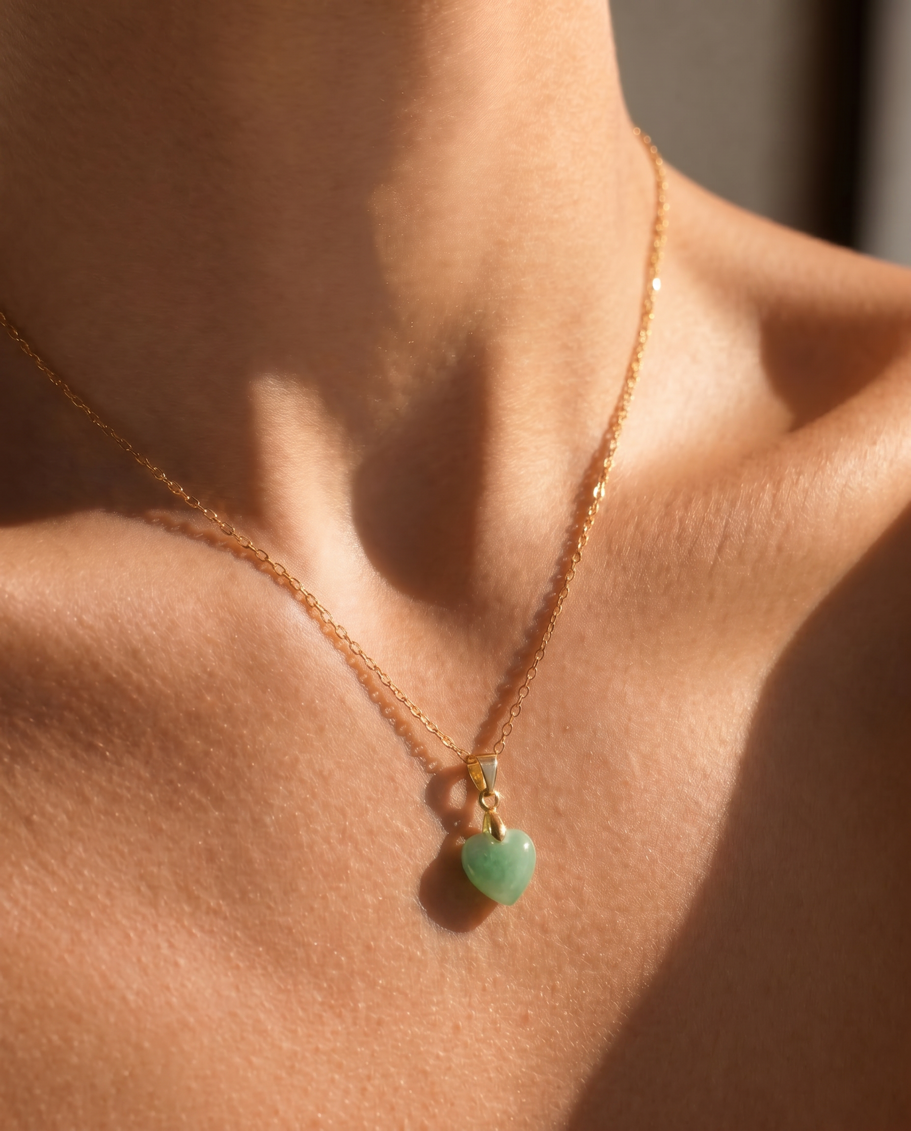 Close-up of a necklace with a tiny green heart-shaped pendant on a person's neck