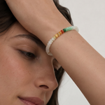Close-up of a person wearing a colorful beaded bracelet on a plain background