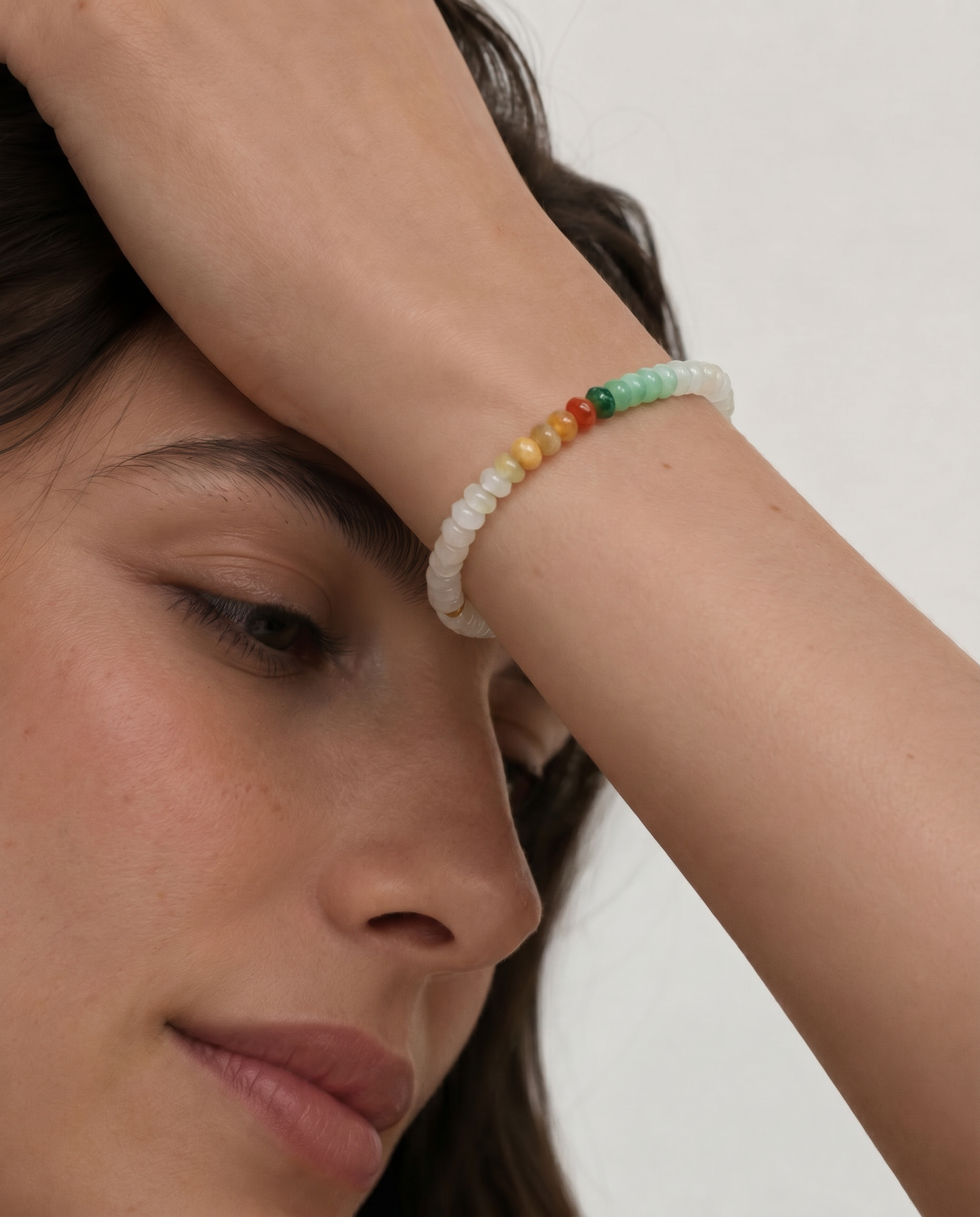 Close-up of a person wearing a colorful beaded bracelet on a plain background